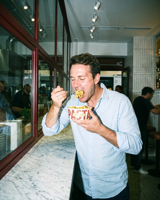 Un ragazzo mangia una bowl di pasta in piedi al banco